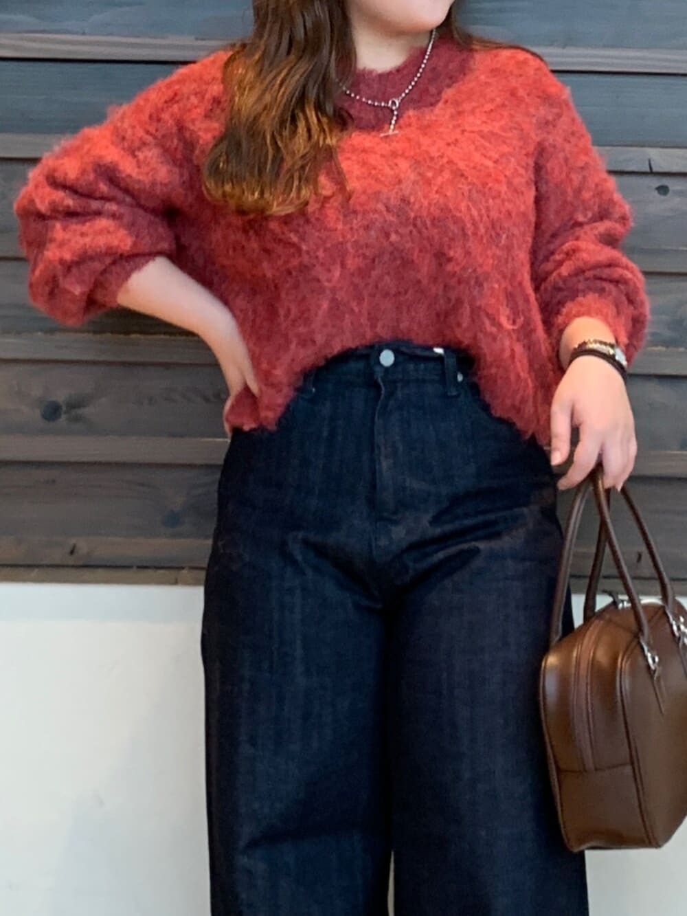 レッド系のニット/セーター、ブルー系のデニムパンツ、ブラウン系のハンドバッグを着用したレディースの秋コーディネートの4枚目の写真