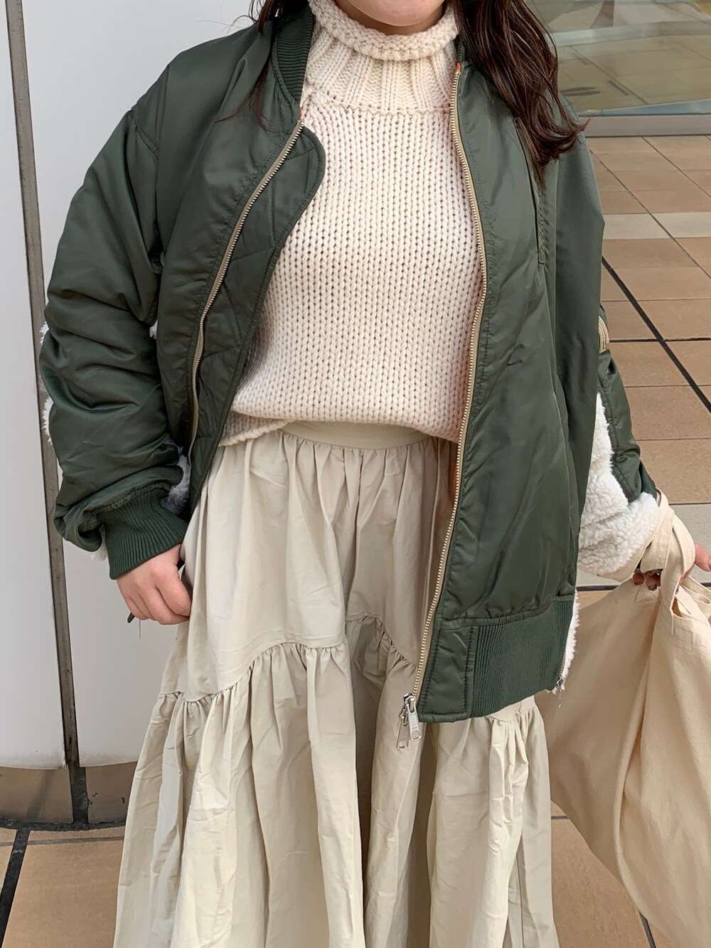 ホワイト系のスカート、ホワイト系のニット/セーター、グリーン系のMA-1を着用したレディースの冬コーディネートの4枚目の写真