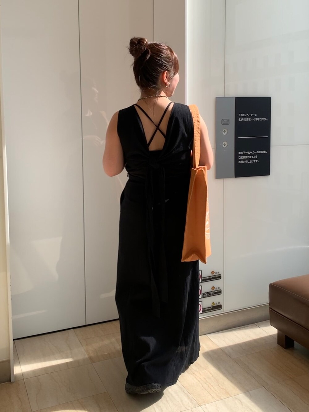 ブラック系のワンピース、オレンジ系のトートバッグを着用したレディースの春コーディネートの3枚目の写真