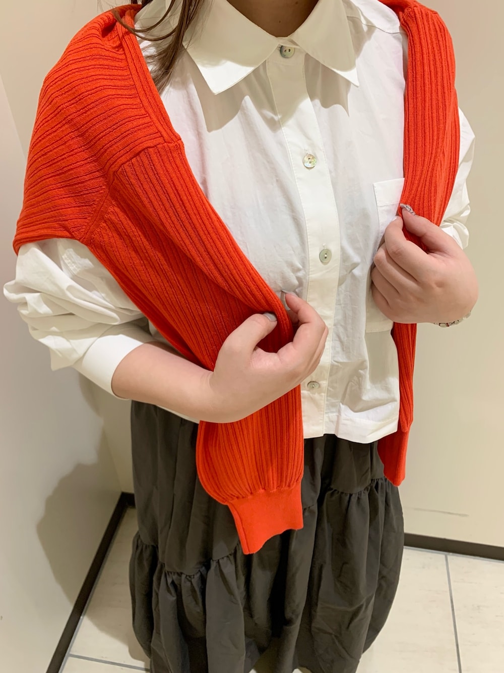 オレンジ系のカーディガン/ボレロ、ホワイト系のシャツ/ブラウス、グレー系のスカートを着用したレディースの春コーディネートの4枚目の写真