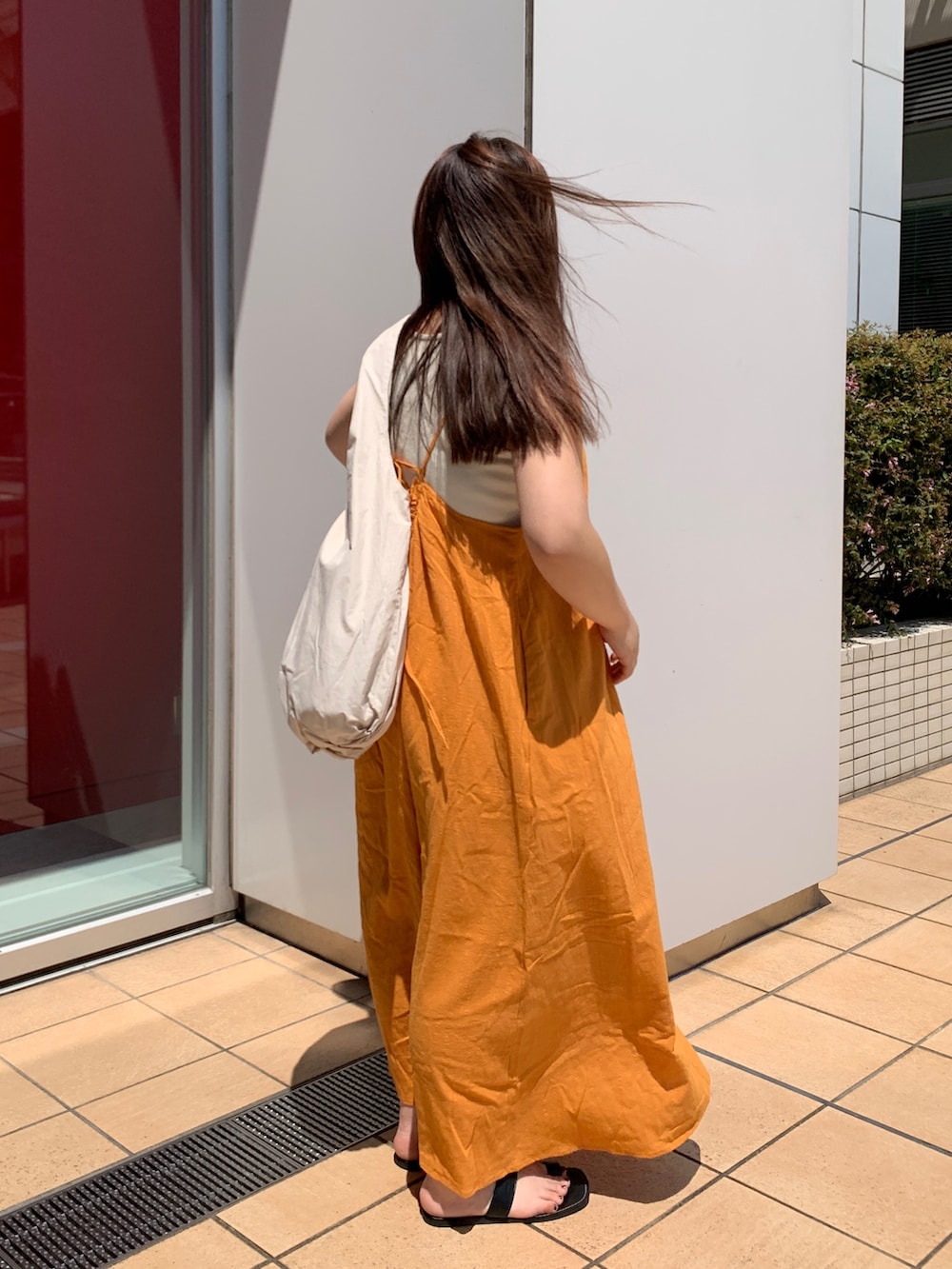 オレンジ系のワンピース、ホワイト系のハンドバッグを着用したレディースの夏コーディネートの2枚目の写真