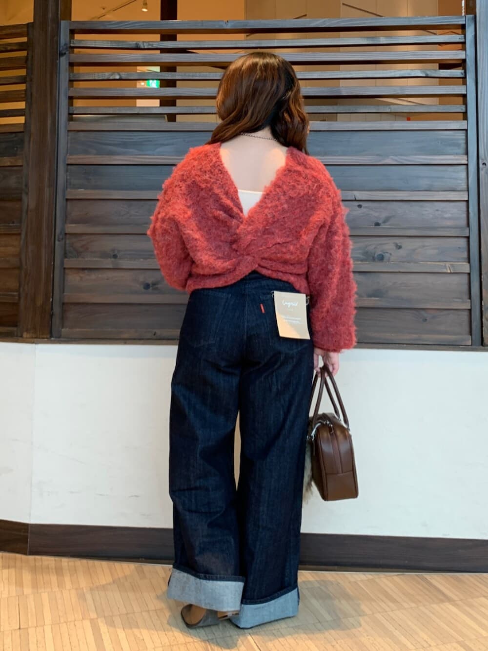 レッド系のニット/セーター、ブルー系のデニムパンツ、ブラウン系のハンドバッグを着用したレディースの秋コーディネートの3枚目の写真