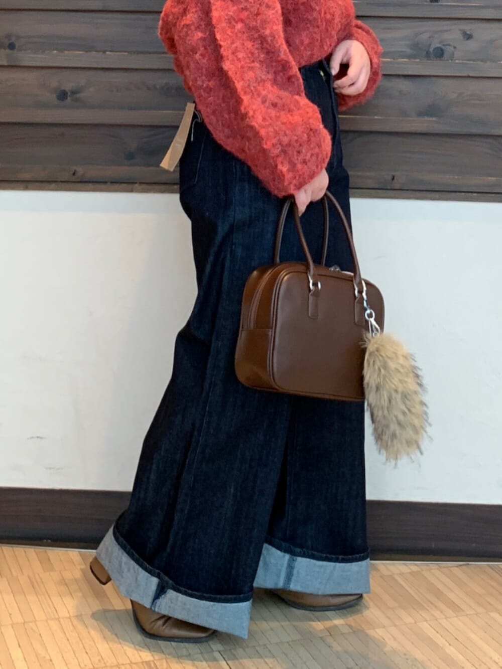 レッド系のニット/セーター、ブルー系のデニムパンツ、ブラウン系のハンドバッグを着用したレディースの秋コーディネートの6枚目の写真