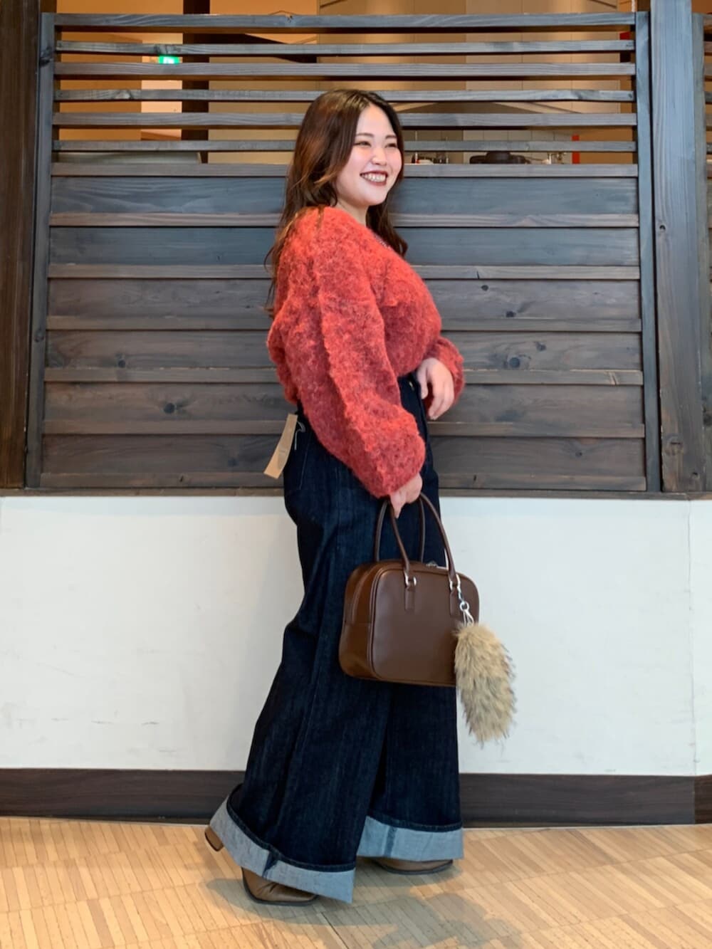 レッド系のニット/セーター、ブルー系のデニムパンツ、ブラウン系のハンドバッグを着用したレディースの秋コーディネートの2枚目の写真
