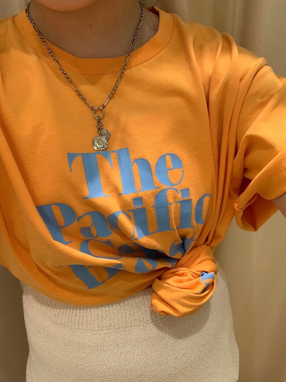 オレンジ系のTシャツ/カットソー、ホワイト系のスカート、ベージュ系のトートバッグを着用したレディースの春コーディネートの4枚目の写真