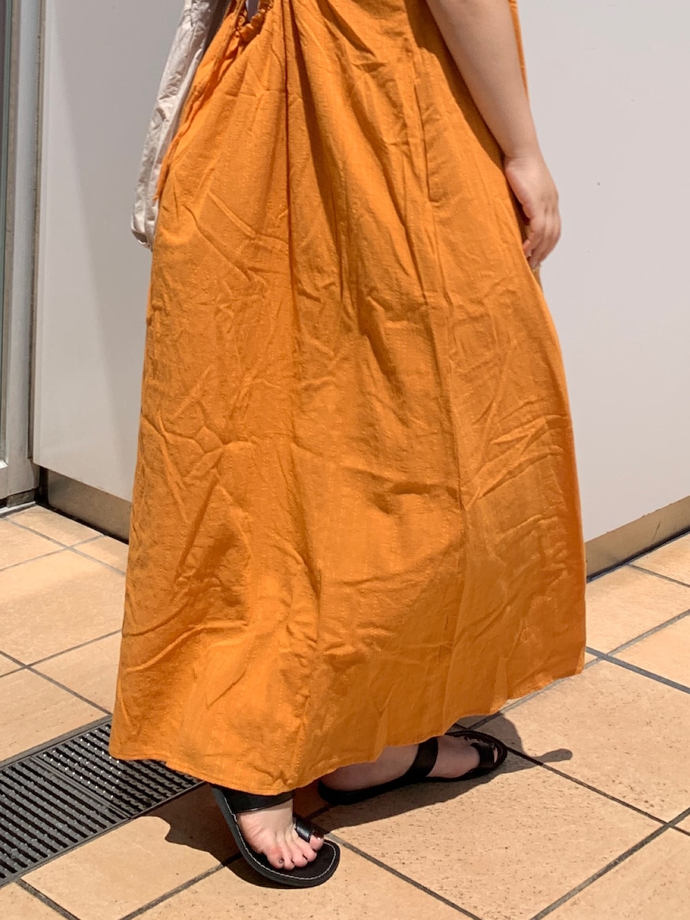 オレンジ系のワンピース、ホワイト系のハンドバッグを着用したレディースの夏コーディネートの6枚目の写真