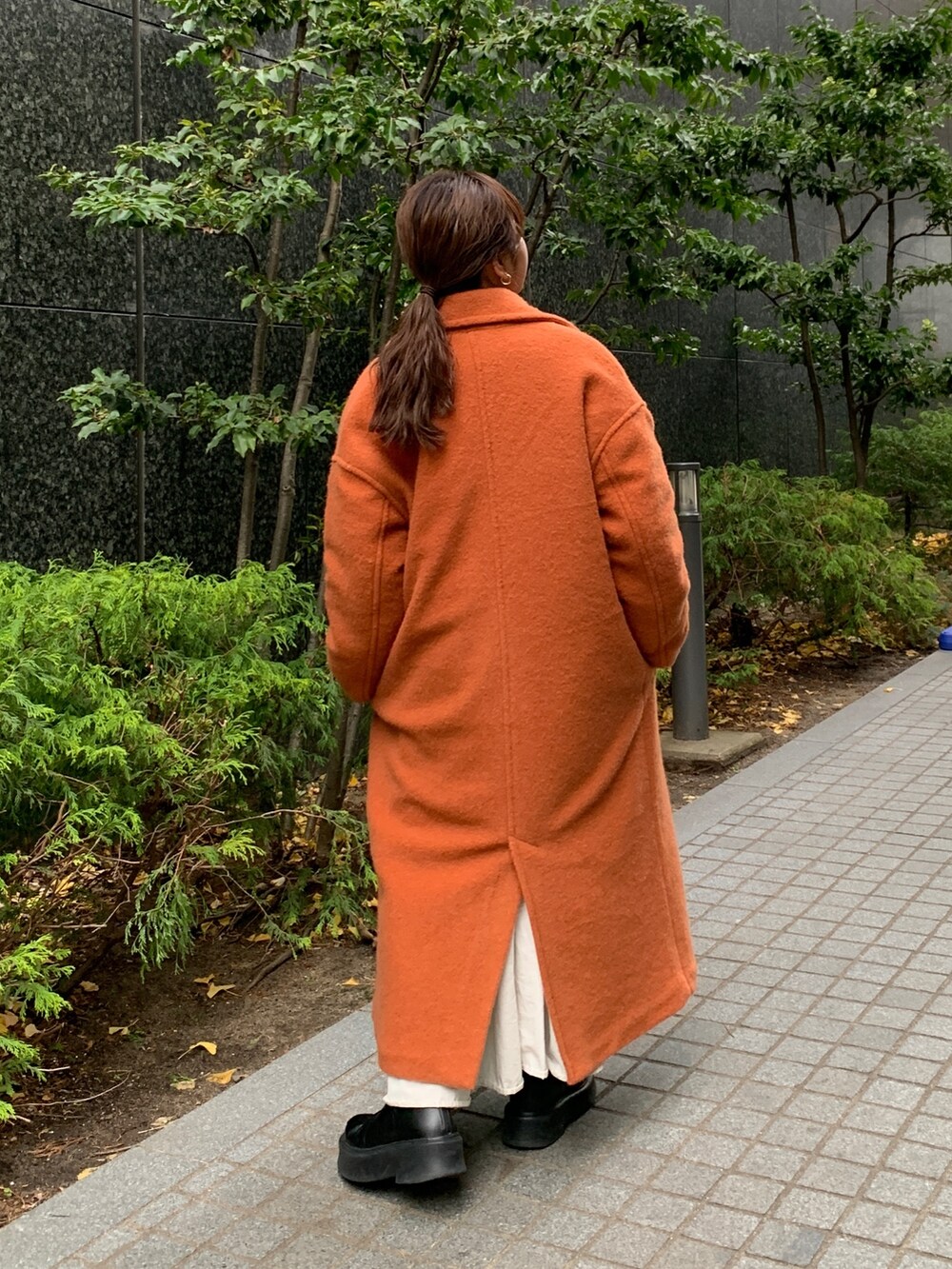 ブラウン系のニット/セーター、ブラック系のワンピース、オレンジ系のチェスターコートを着用したレディースの冬コーディネートの3枚目の写真