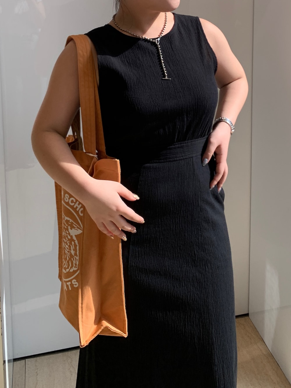 ブラック系のワンピース、オレンジ系のトートバッグを着用したレディースの春コーディネートの4枚目の写真