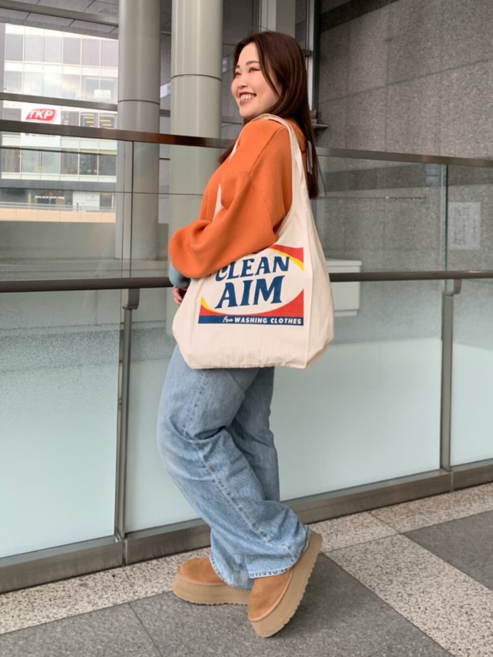 オレンジ系のニット/セーター、ブルー系のデニムパンツ、ホワイト系のトートバッグを着用したレディースの冬コーディネートの2枚目の写真