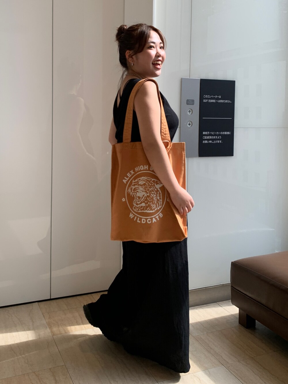 ブラック系のワンピース、オレンジ系のトートバッグを着用したレディースの春コーディネートの2枚目の写真