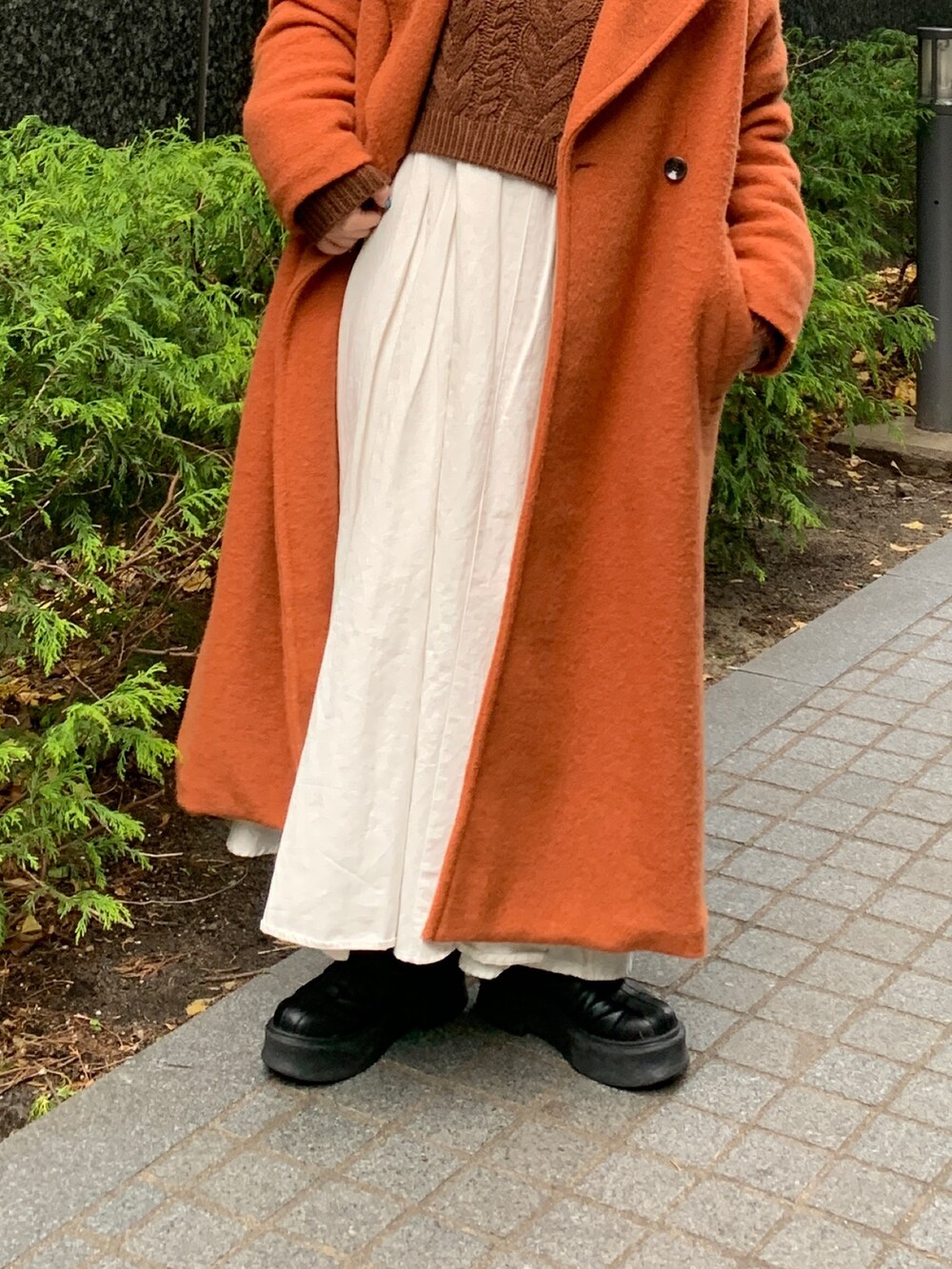 ブラウン系のニット/セーター、ブラック系のワンピース、オレンジ系のチェスターコートを着用したレディースの冬コーディネートの4枚目の写真