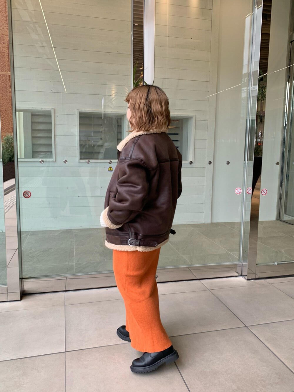 ブラウン系のムートンコート、オレンジ系のスカート、ホワイト系のニット/セーターを着用したレディースの冬コーディネートの2枚目の写真