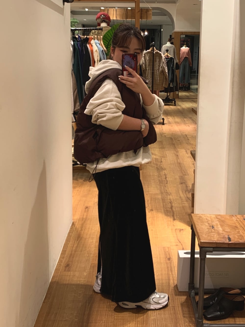 ブラウン系のダウンベスト、ホワイト系のパーカー、ブラック系のスカートを着用したレディースの秋コーディネートの2枚目の写真