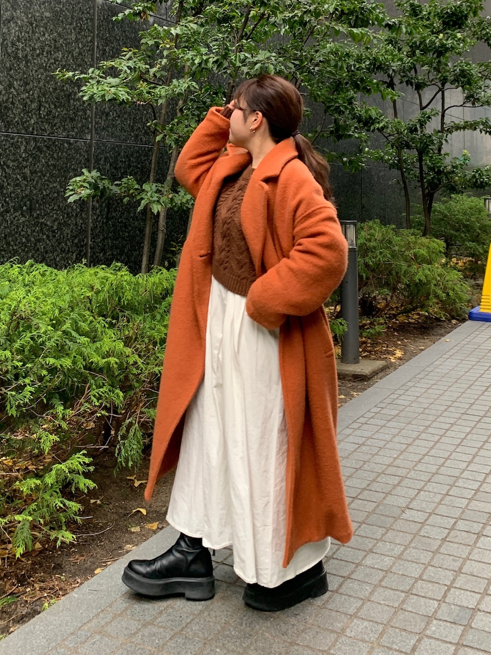 ブラウン系のニット/セーター、ブラック系のワンピース、オレンジ系のチェスターコートを着用したレディースの冬コーディネートの2枚目の写真