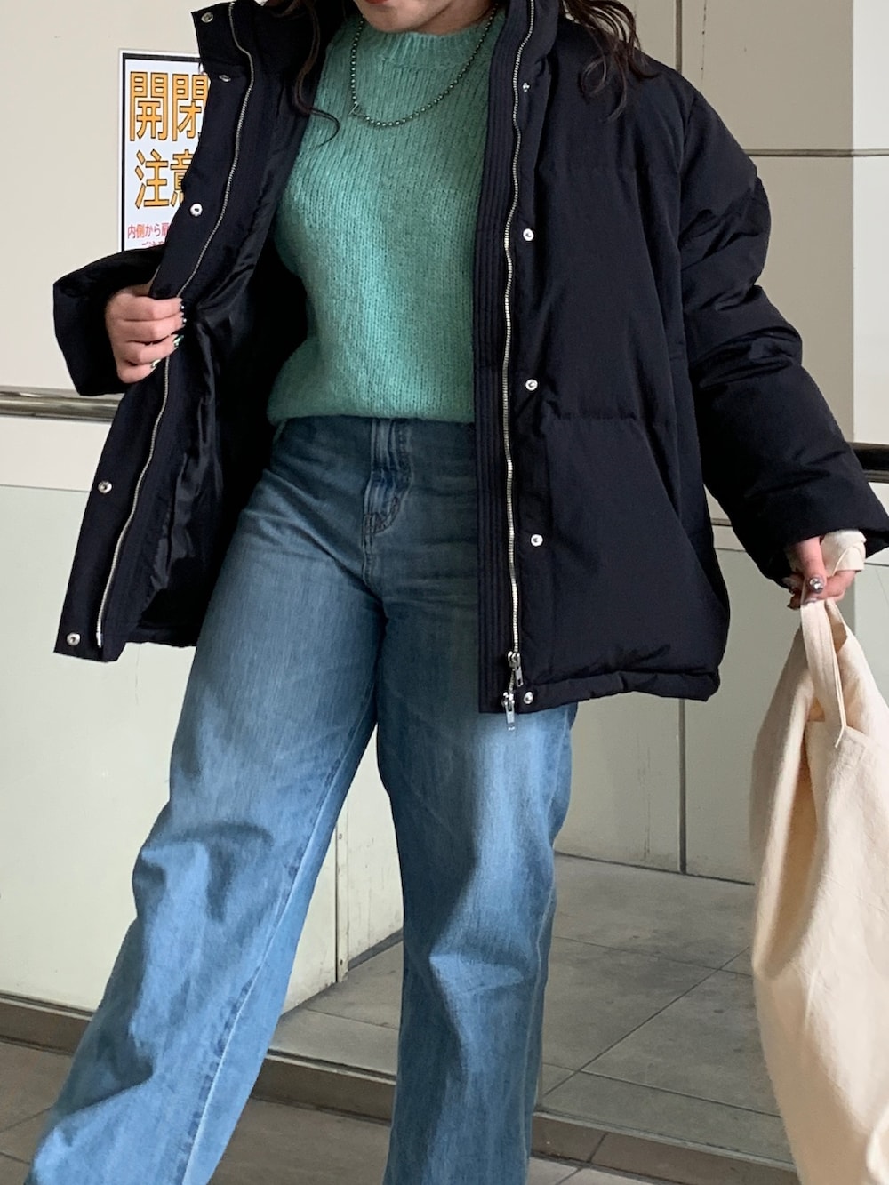 ブラック系のダウンジャケット/コート、グリーン系のニット/セーター、ブルー系のデニムパンツを着用したレディースの冬コーディネートの4枚目の写真