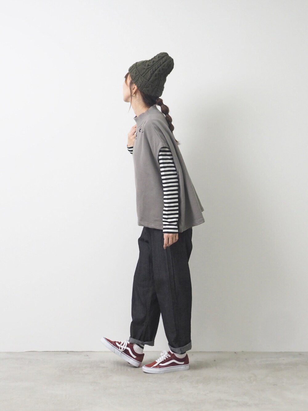 グレー系のベスト、ブラック系のデニムパンツ、レッド系のスニーカーを着用したレディースの秋コーディネートの2枚目の写真