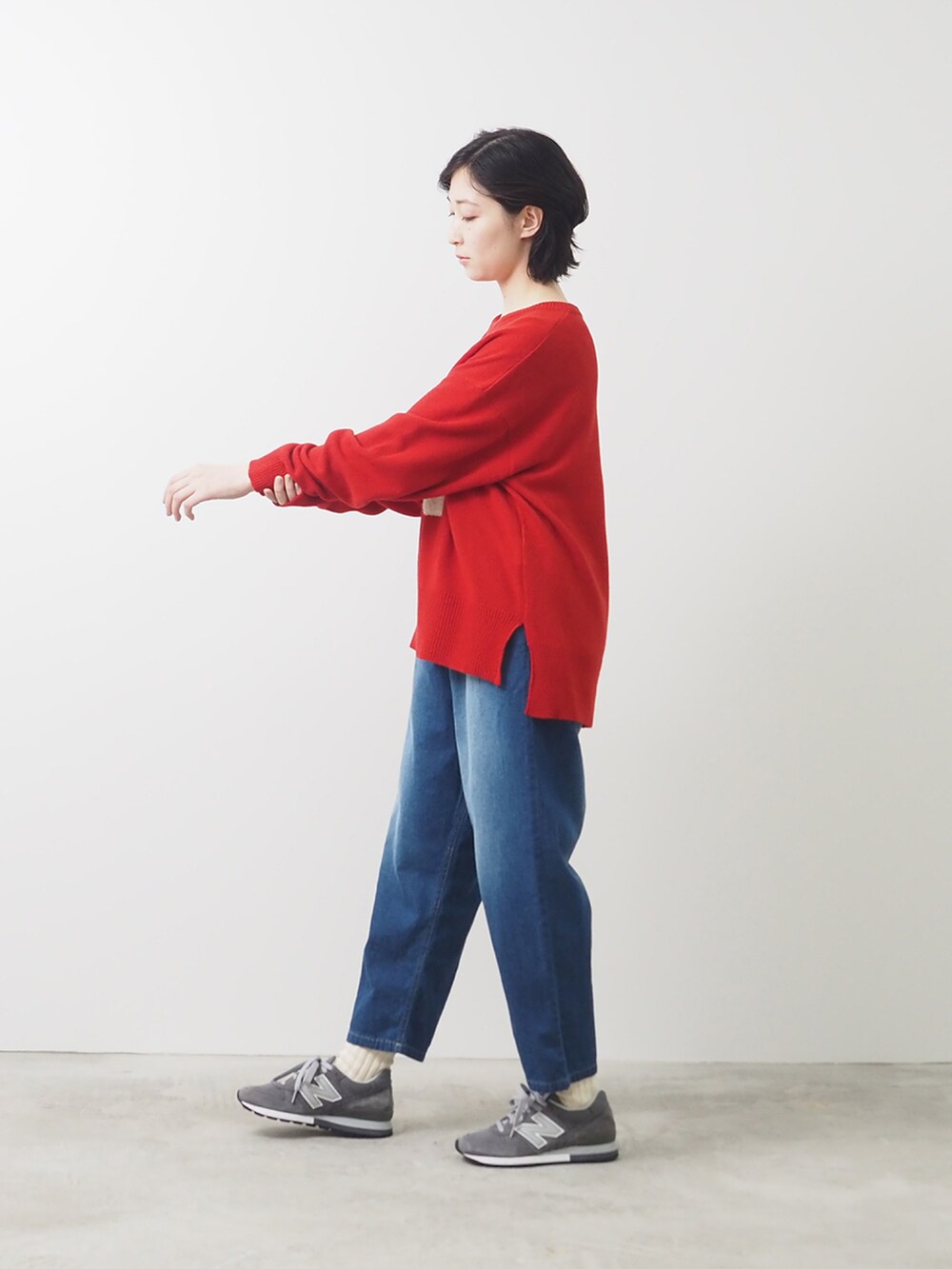 レッド系のニット/セーター、ブルー系のデニムパンツを着用したレディースの秋コーディネートの2枚目の写真