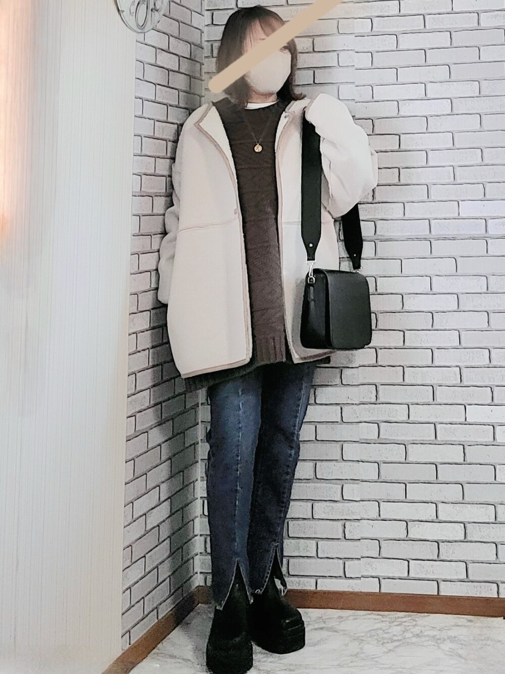 ホワイト系のムートンコート、ブラウン系のニット/セーター、ホワイト系のTシャツ/カットソーを着用したレディースの冬コーディネートの2枚目の写真