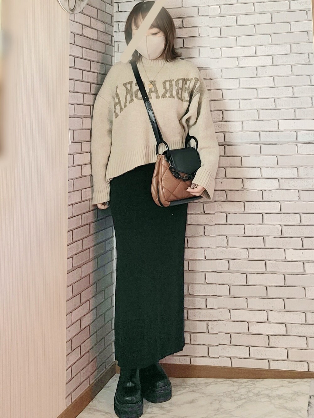 ブラック系のノーカラーコート、ベージュ系のニット/セーター、ブラック系のスカートを着用したレディースの冬コーディネートの2枚目の写真