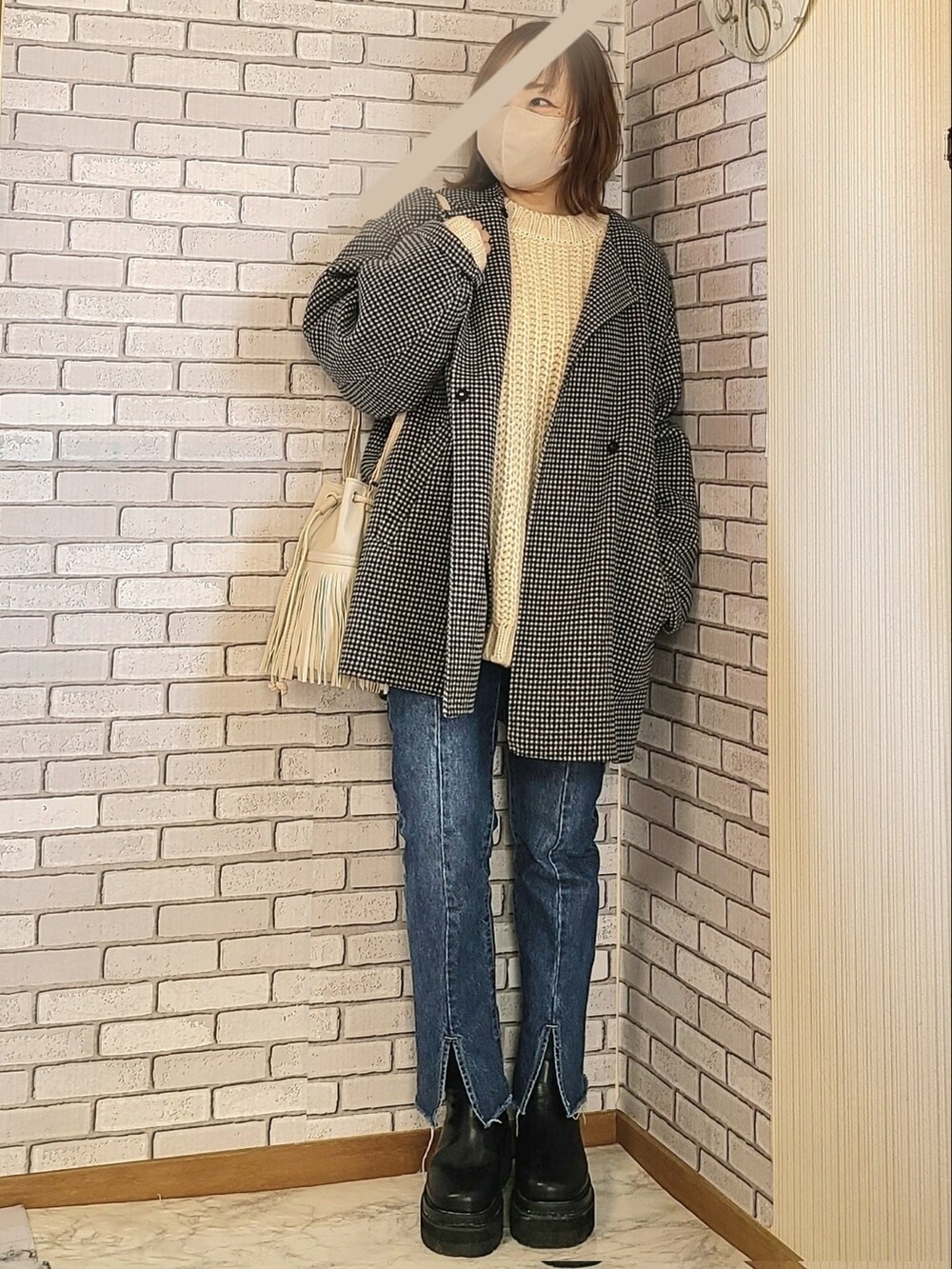 ブラック系のノーカラーコート、ベージュ系のニット/セーター、ブルー系のデニムパンツを着用したレディースの冬コーディネートの2枚目の写真