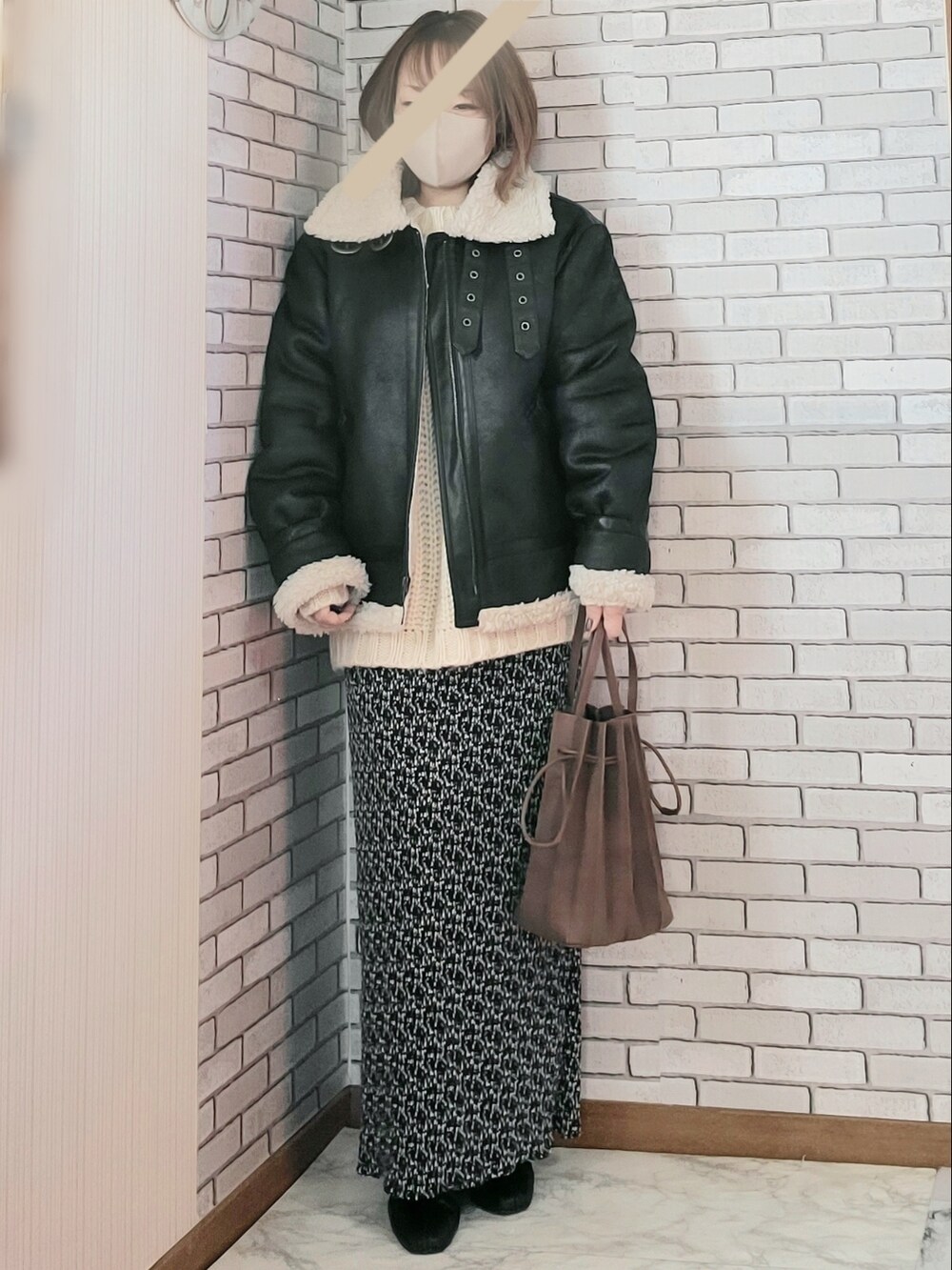 ブラック系のムートンコート、ベージュ系のニット/セーター、ブラック系のスカートを着用したレディースの冬コーディネートの2枚目の写真