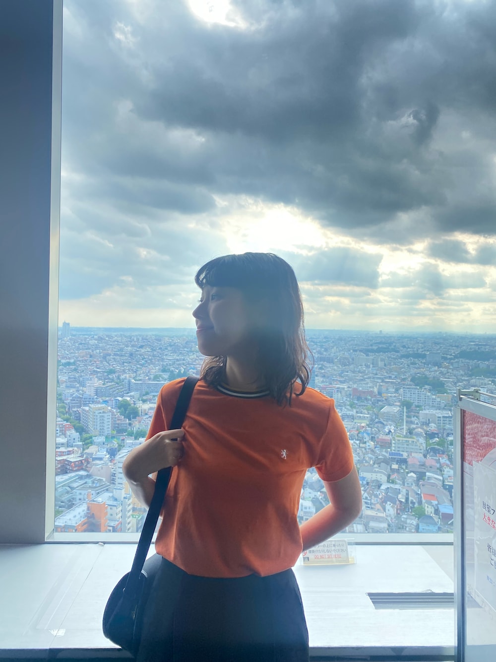 オレンジ系のTシャツ/カットソー、ブラック系のショルダーバッグ、ブラック系のパンツを着用したレディースの夏コーディネートの3枚目の写真