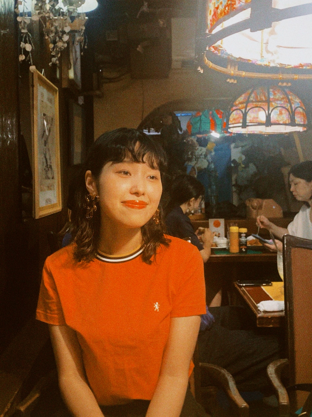 オレンジ系のTシャツ/カットソー、ブラック系のショルダーバッグ、ブラック系のパンツを着用したレディースの夏コーディネートの2枚目の写真