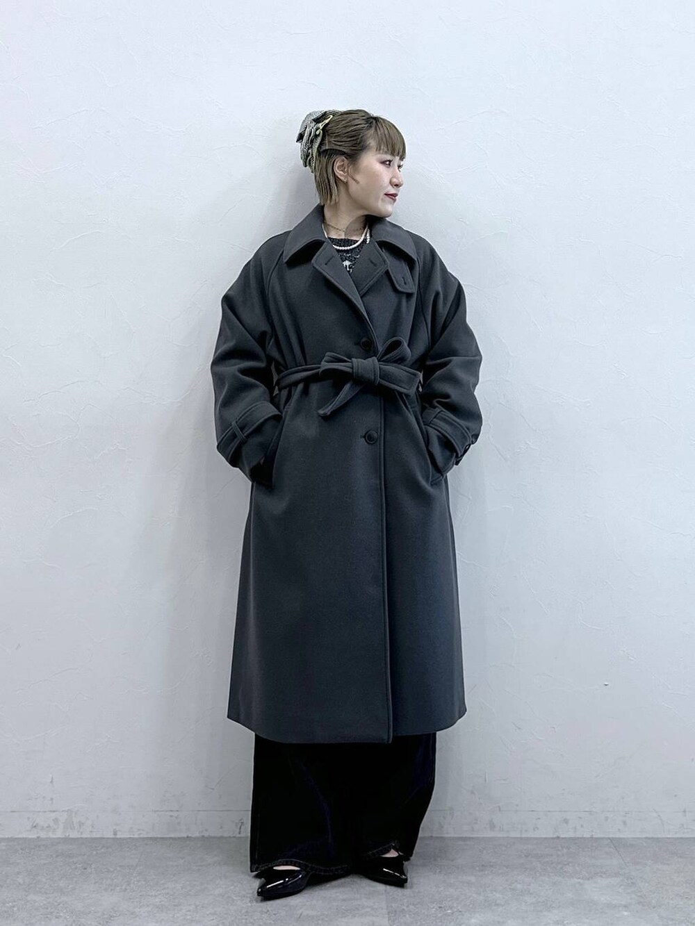 グレー系のステンカラーコート、ブラック系のニット/セーター、ブラック系のパンプスを着用したレディースの冬コーディネートの2枚目の写真