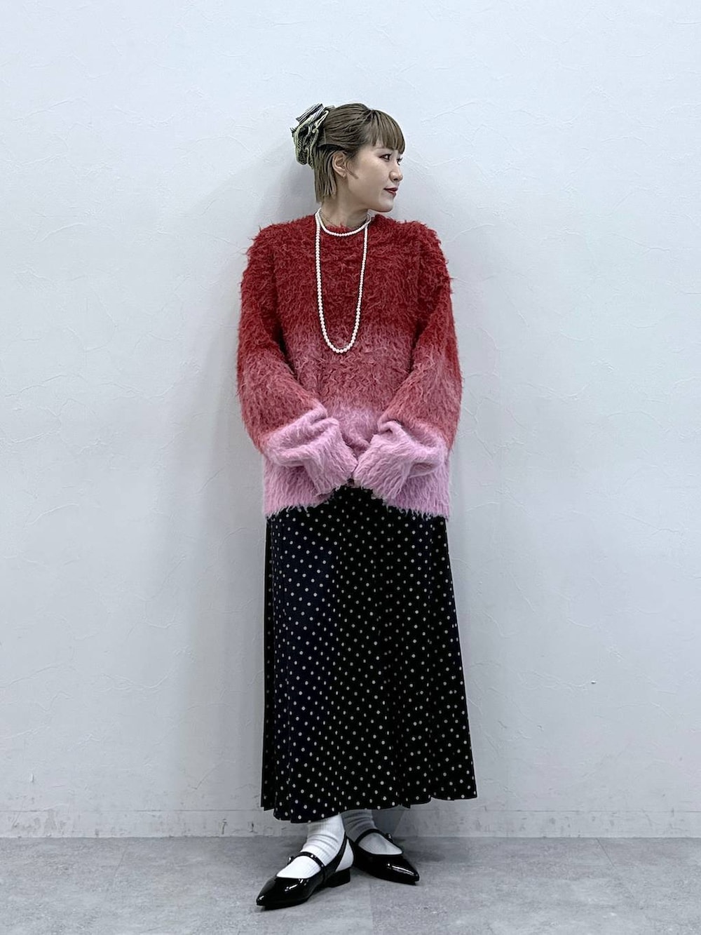 レッド系のニット/セーター、ブラック系のパンプス、ブラック系のスカートを着用したレディースの冬コーディネートの2枚目の写真