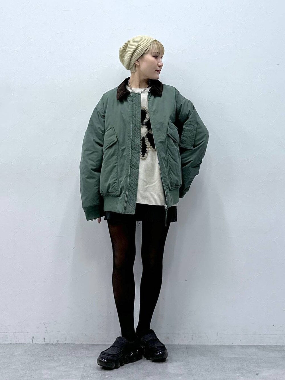 グレー系のスカート、ホワイト系のニット/セーター、グリーン系のブルゾンを着用したレディースの冬コーディネートの3枚目の写真