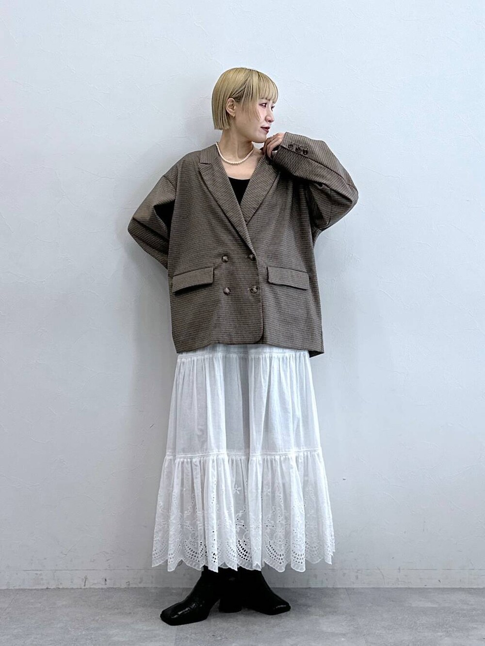 ブラウン系のテーラードジャケット、ホワイト系のスカート、ブラック系のブラジャーを着用したレディースの秋コーディネートの2枚目の写真