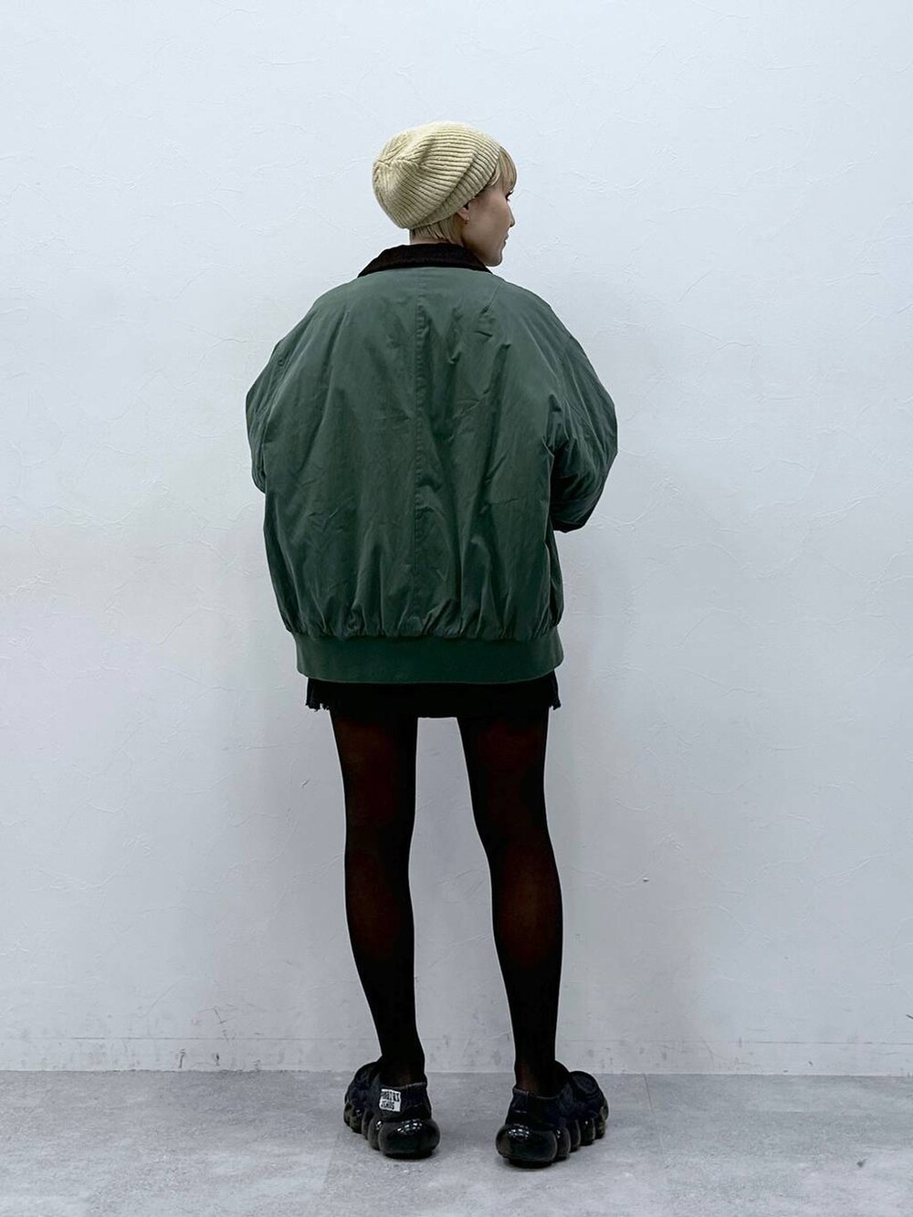 グレー系のスカート、ホワイト系のニット/セーター、グリーン系のブルゾンを着用したレディースの冬コーディネートの5枚目の写真