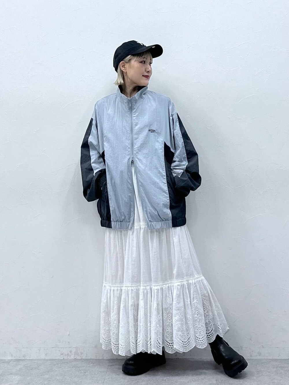 グレー系のブルゾン、ホワイト系のスカート、ブラック系のブーツを着用したレディースの秋コーディネートの2枚目の写真