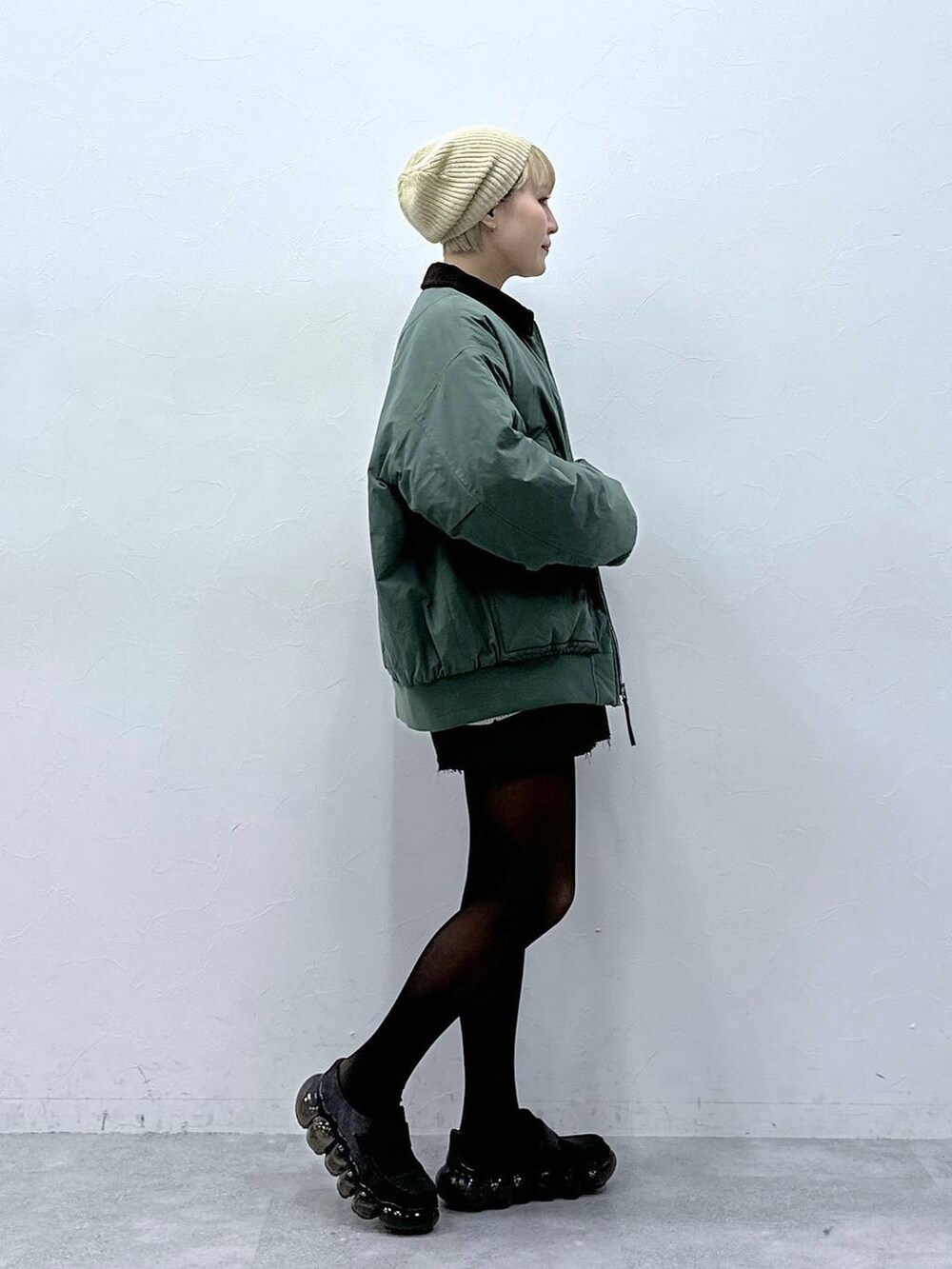 グレー系のスカート、ホワイト系のニット/セーター、グリーン系のブルゾンを着用したレディースの冬コーディネートの4枚目の写真