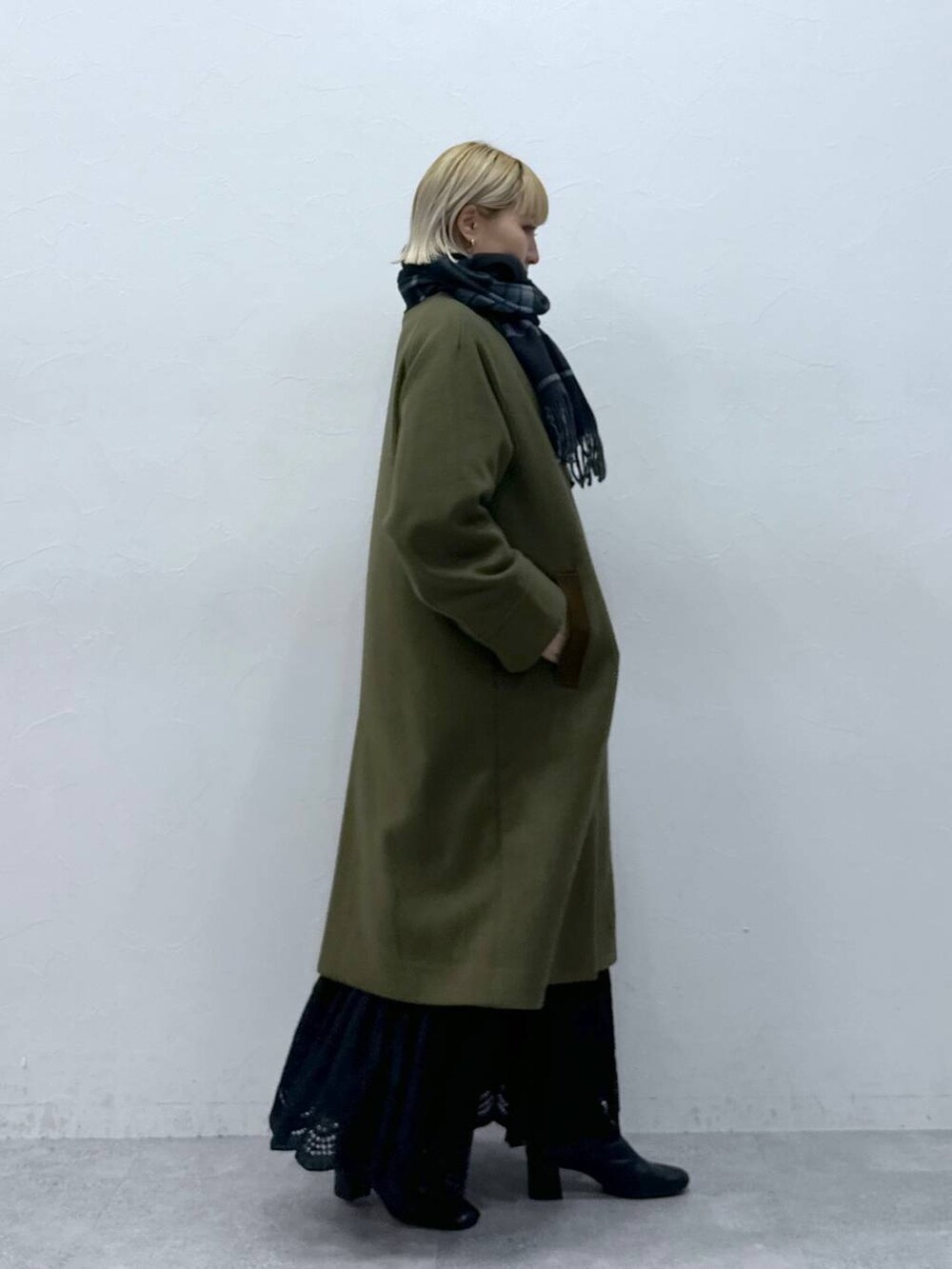 グリーン系のステンカラーコート、ホワイト系のスカート、ブラック系のマフラーを着用したレディースの秋コーディネートの2枚目の写真