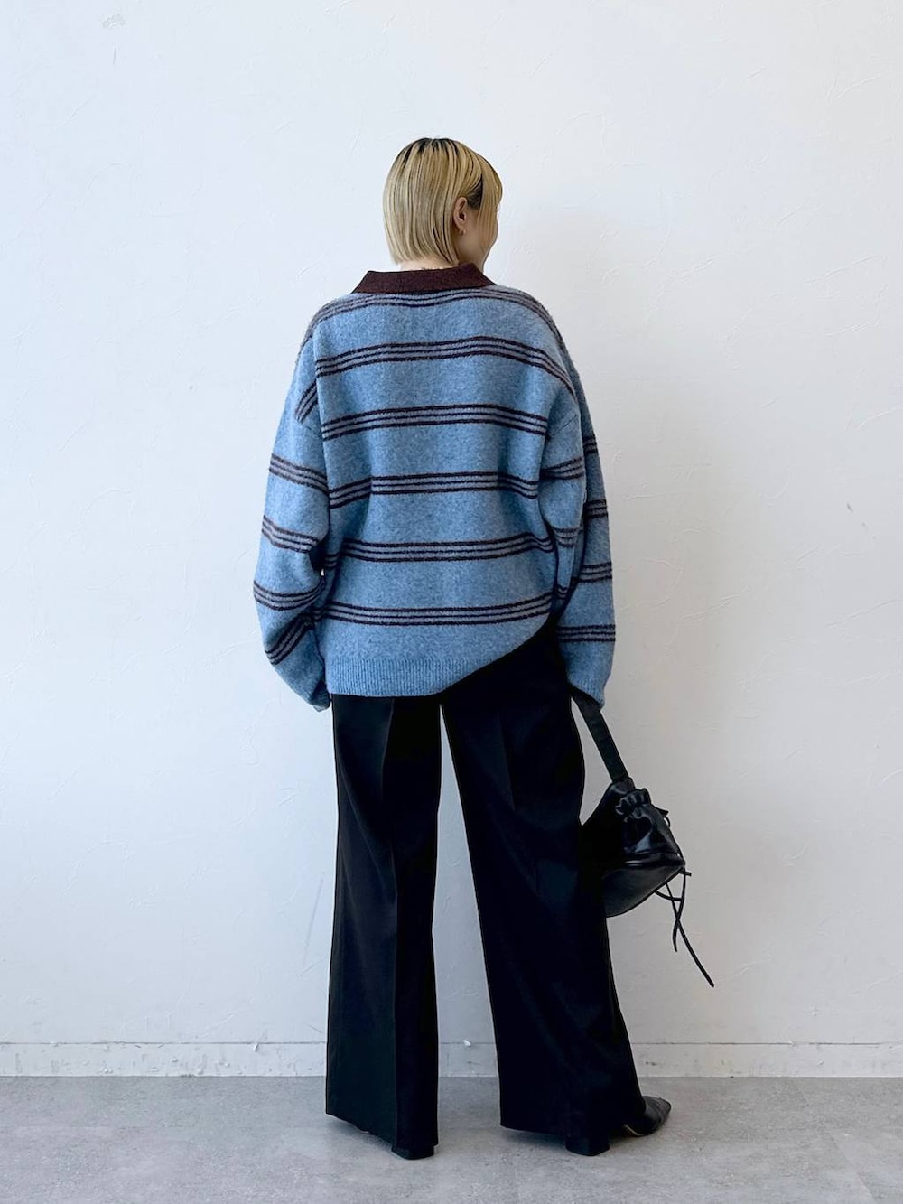 ブラック系のショルダーバッグ、ブラウン系のスラックス、ブルー系のポロシャツを着用したレディースの冬コーディネートの5枚目の写真