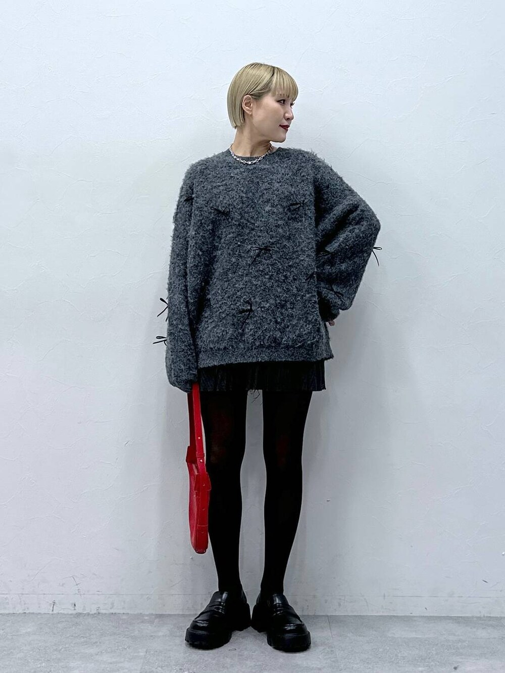 グレー系のスカート、レッド系のショルダーバッグ、グレー系のニット/セーターを着用したレディースの冬コーディネートの2枚目の写真