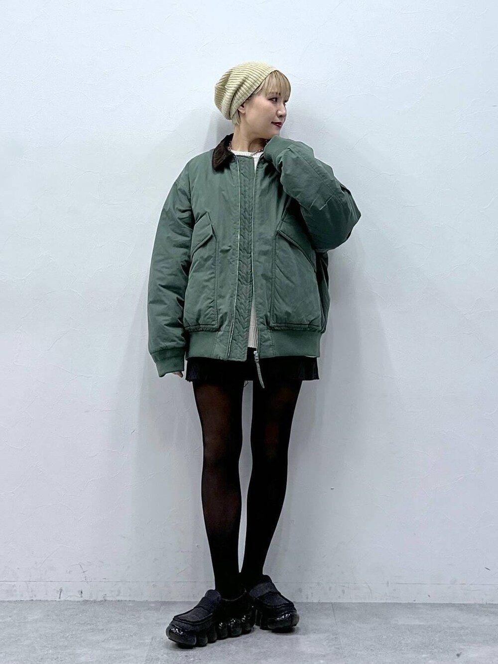 グレー系のスカート、ホワイト系のニット/セーター、グリーン系のブルゾンを着用したレディースの冬コーディネートの6枚目の写真