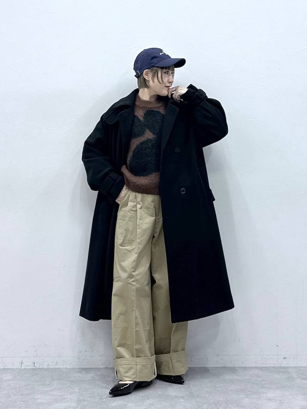 ブラック系のステンカラーコート、ブラウン系のニット/セーター、ベージュ系のチノパンツを着用したレディースの冬コーディネートの5枚目の写真