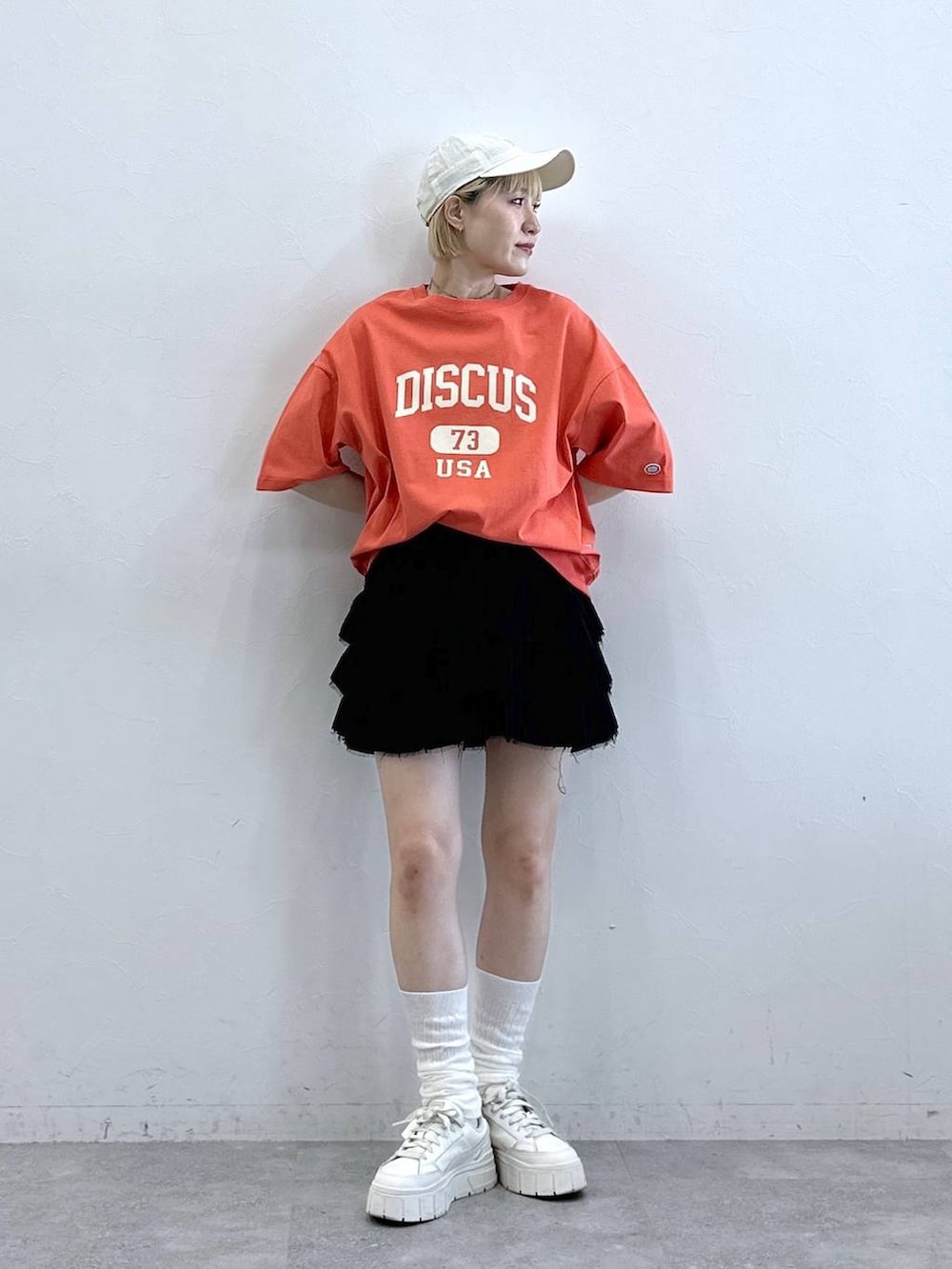 レッド系のTシャツ/カットソー、ブラック系のスカート、ホワイト系のキャップを着用したレディースの春コーディネートの2枚目の写真