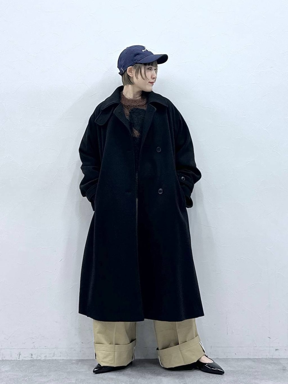 ブラック系のステンカラーコート、ブラウン系のニット/セーター、ベージュ系のチノパンツを着用したレディースの冬コーディネートの4枚目の写真