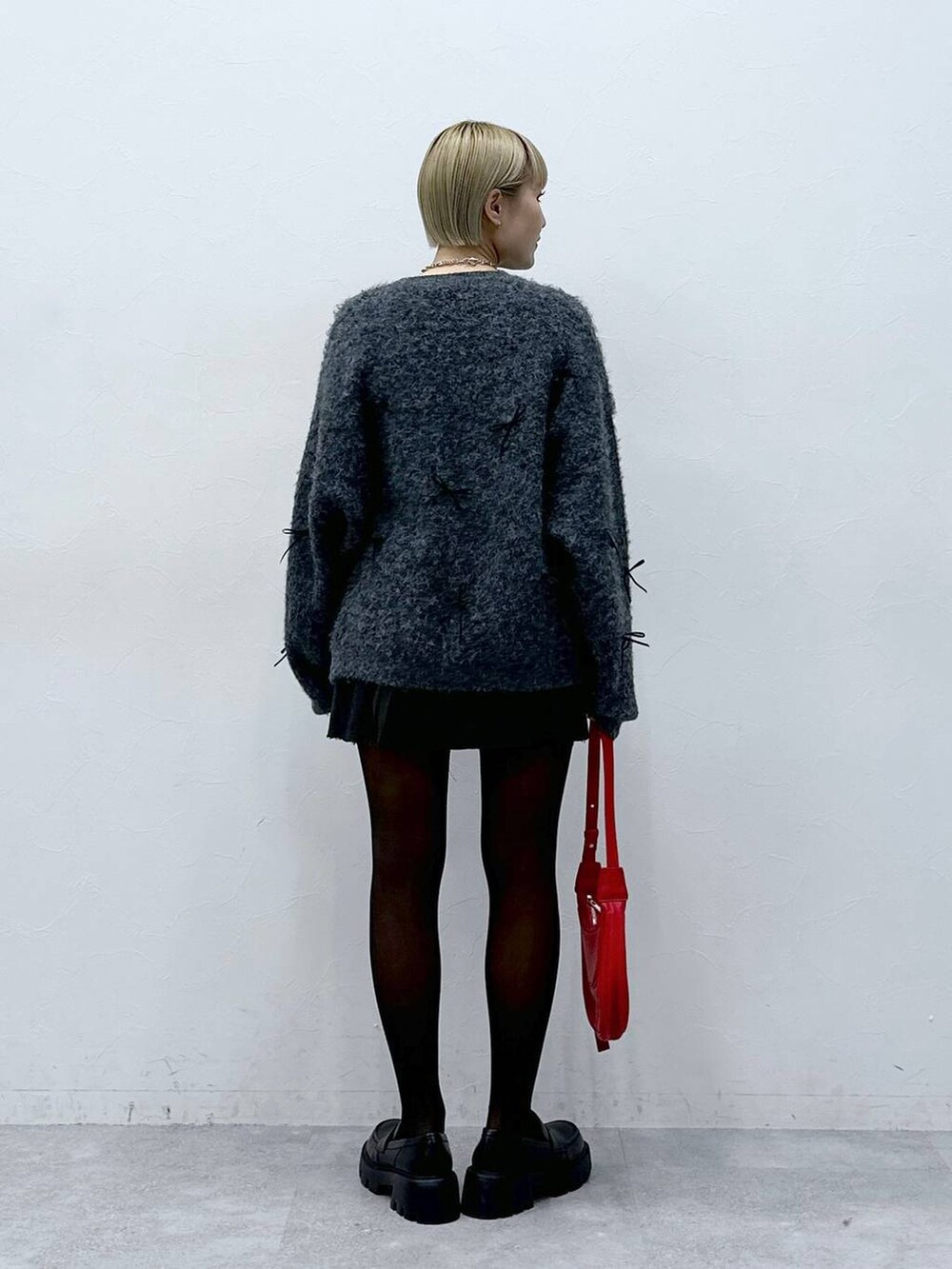 グレー系のスカート、レッド系のショルダーバッグ、グレー系のニット/セーターを着用したレディースの冬コーディネートの4枚目の写真