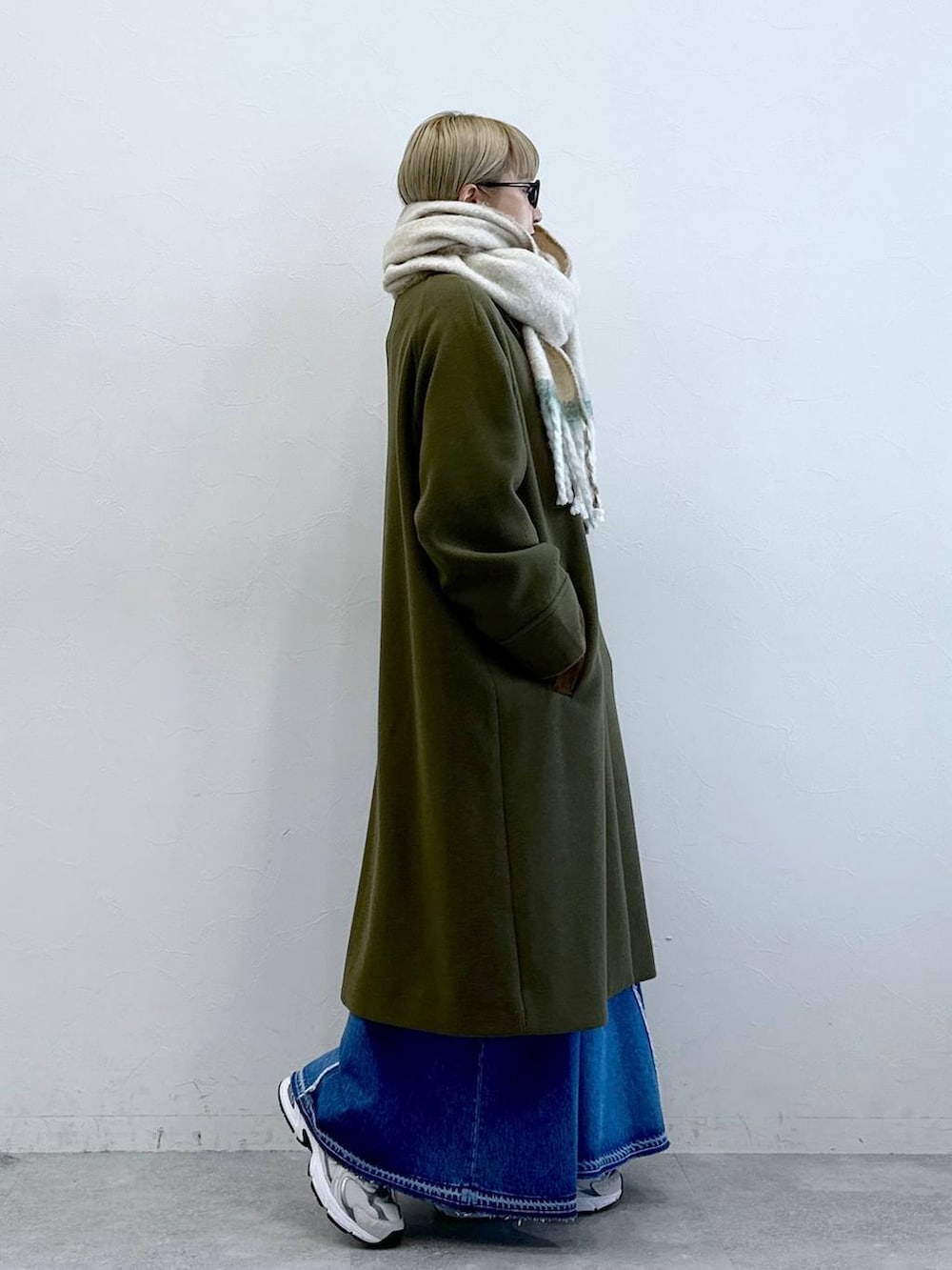 グリーン系のステンカラーコート、ブルー系のデニムスカート、ブラック系のサングラスを着用したレディースの冬コーディネートの3枚目の写真