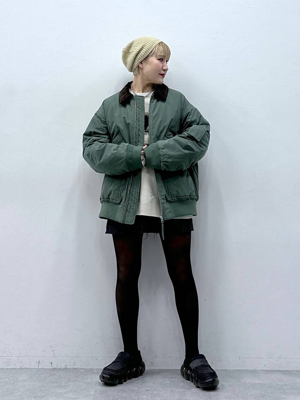 グレー系のスカート、ホワイト系のニット/セーター、グリーン系のブルゾンを着用したレディースの冬コーディネートの2枚目の写真