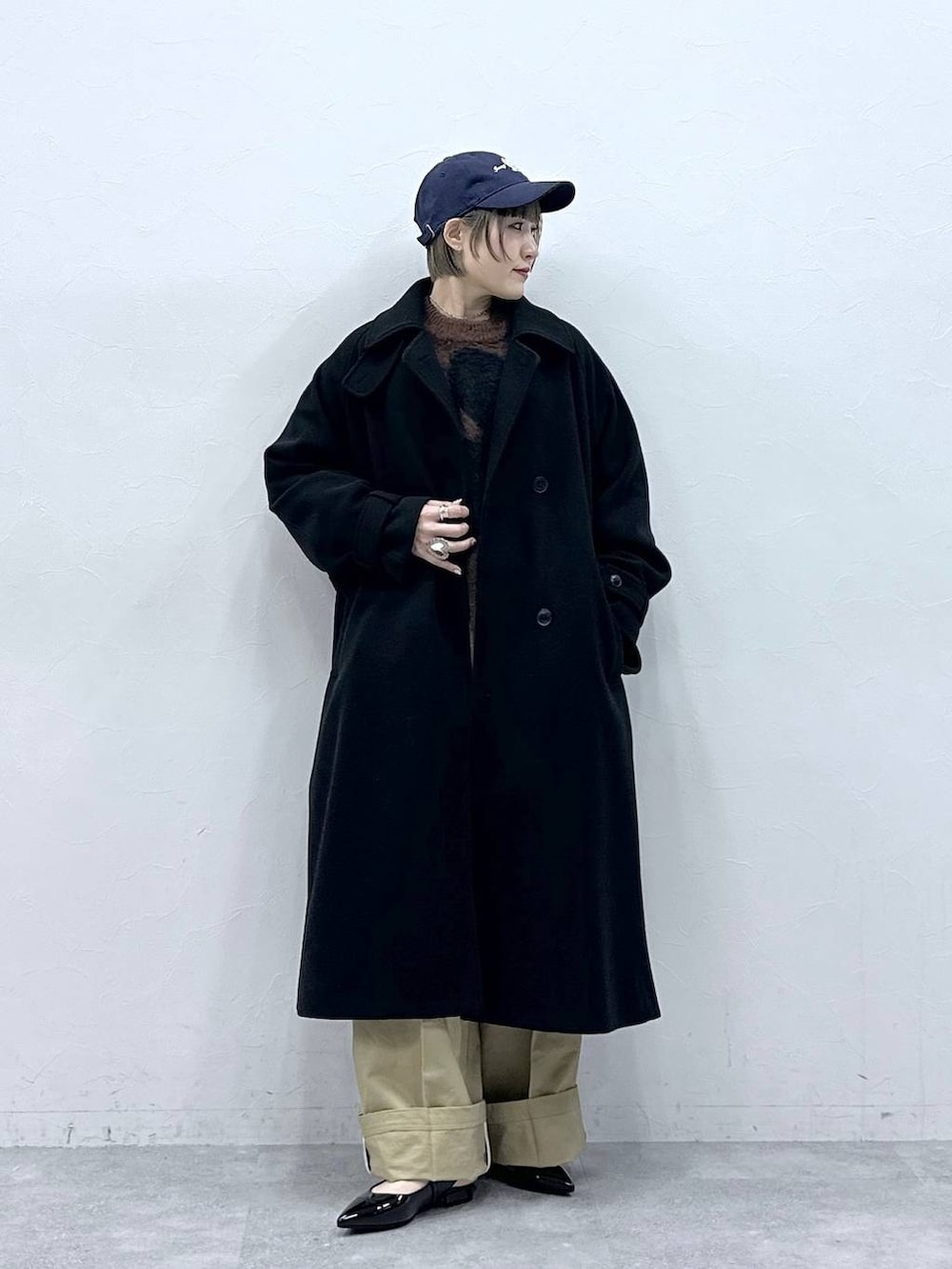 ブラック系のステンカラーコート、ブラウン系のニット/セーター、ベージュ系のチノパンツを着用したレディースの冬コーディネートの3枚目の写真