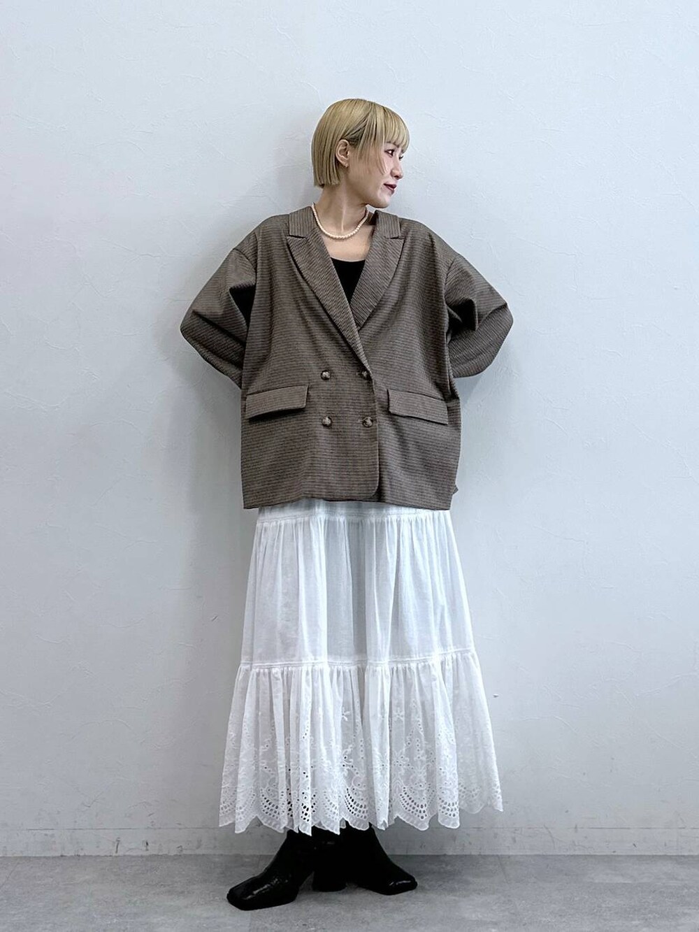 ブラウン系のテーラードジャケット、ホワイト系のスカート、ブラック系のブラジャーを着用したレディースの秋コーディネートの3枚目の写真