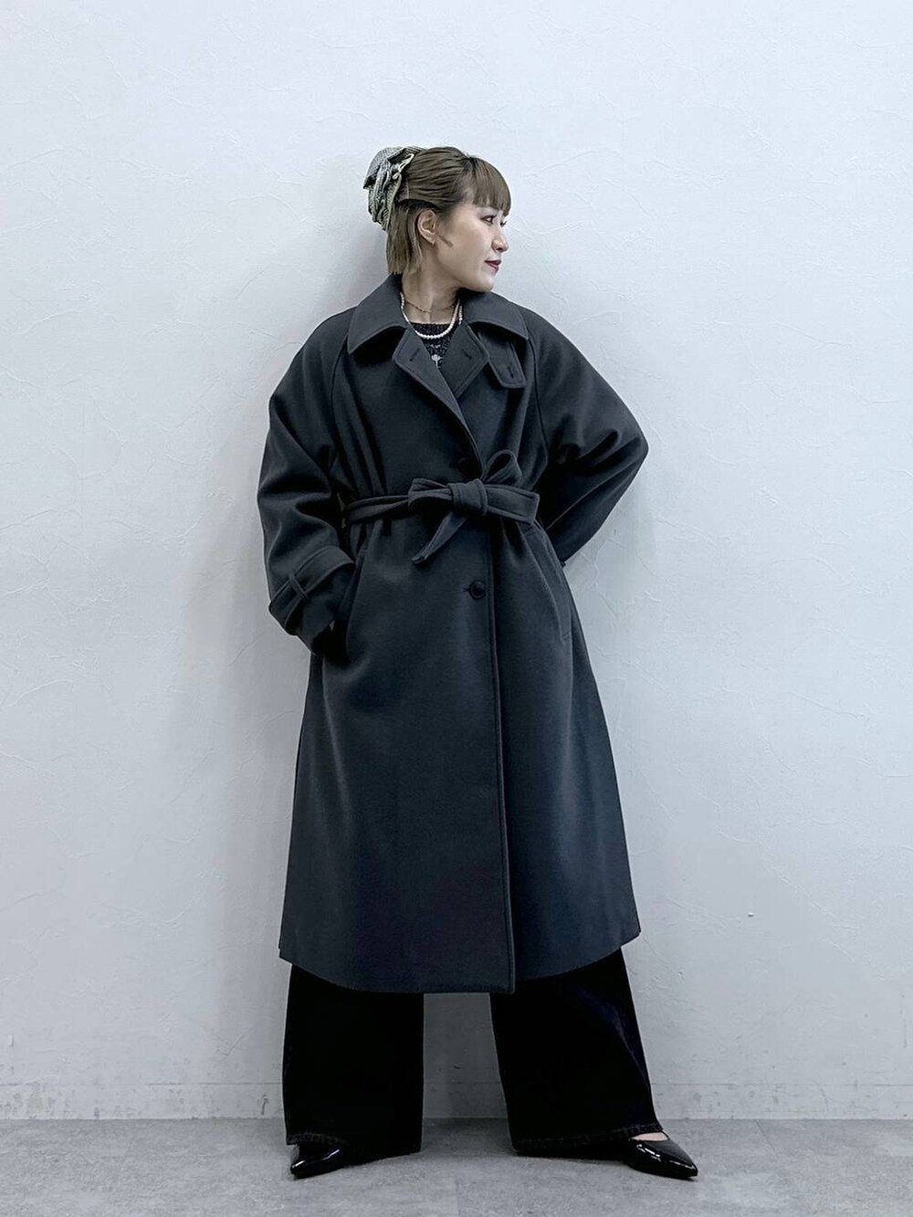 グレー系のステンカラーコート、ブラック系のニット/セーター、ブラック系のパンプスを着用したレディースの冬コーディネートの3枚目の写真