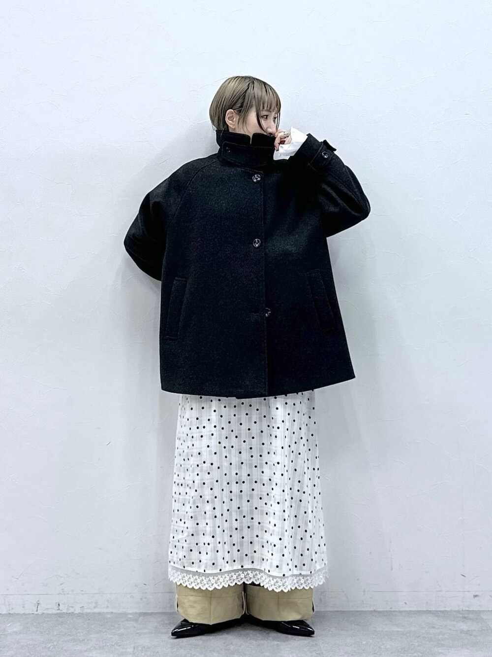 ブラック系のパンプス、ブラック系のステンカラーコート、ベージュ系のチノパンツを着用したレディースの冬コーディネートの2枚目の写真