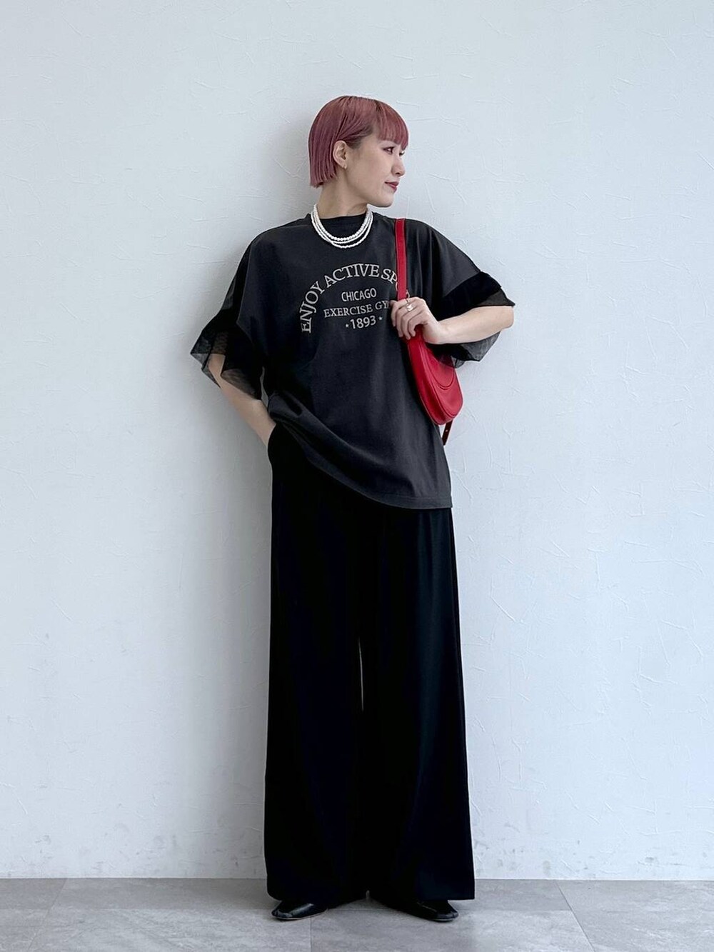 レッド系のショルダーバッグ、ブラック系のスラックス、ブラック系のTシャツ/カットソーを着用したレディースの春コーディネートの2枚目の写真