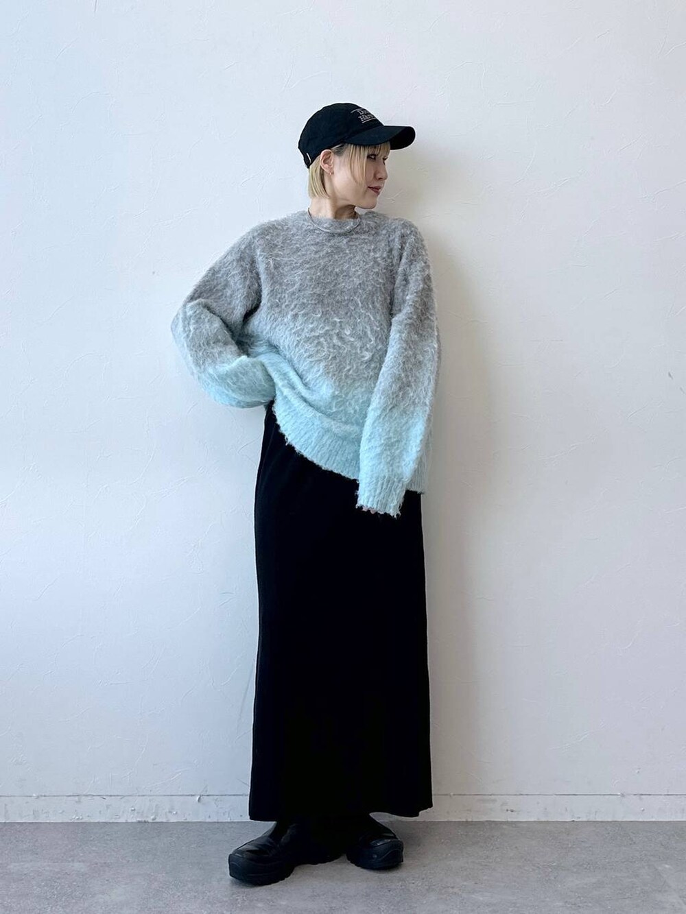 グレー系のニット/セーター、ブラック系のスカート、ブラック系のキャップを着用したレディースの秋コーディネートの2枚目の写真